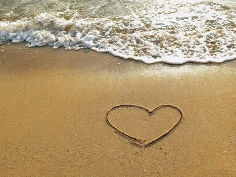 Heart drawn on the sand of a sea beach with white wave at sunset time.