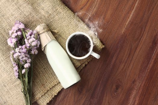 hot dark coffee with smoke and fresh milk in the bottle on sack background over wooden table decorated with beautiful flower bouquet, top view