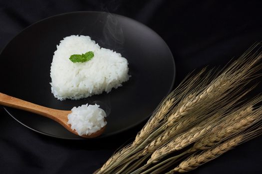hot cook jasmine rice on spoon serve with smoke. rice heart shape on black dish for background. selective focus