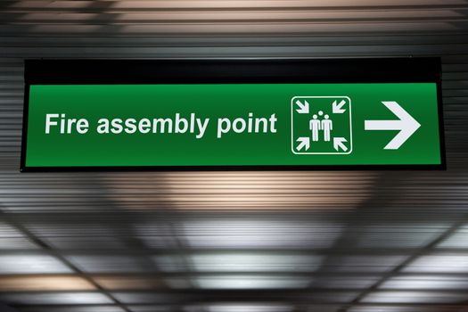 green fire assembly point sign hanging from ceiling