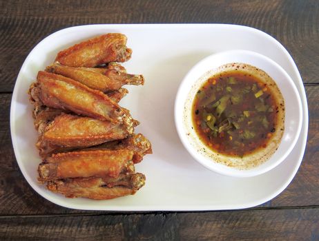 lots of fired chicken wing with sauce on a white plate with wooden background ,top view