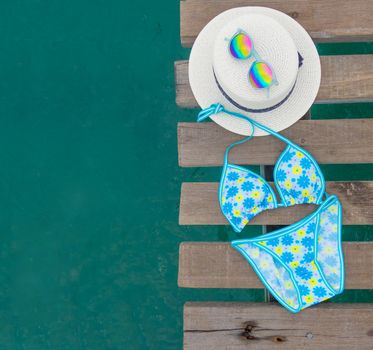 Set of beach clothes. Blue bikini colorful with flowers , hat and sunglasses on wooden bridge over the sea surface. Summer accessories set for background