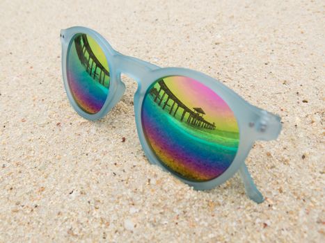 Fashion blue frame sunglasses on sandy sea beach with mirror lenses. Sea beach reflection on black fashion sunglasses. Summer holiday relax background with copy space.