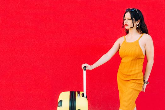 young woman holding suitcase and smiling while standing.