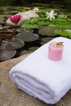 pink candle on white bath towel as spa set near lotus pond in the garden