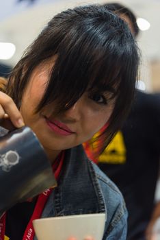 Bangkok, Thailand - June 3, 2017 : Unidentified woman barista pouring latte froth to make a coffee latte art into the white coffee cup for serve to customers in the coffee shop.