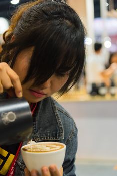 Bangkok, Thailand - June 3, 2017 : Unidentified woman barista pouring latte froth to make a coffee latte art into the white coffee cup for serve to customers in the coffee shop.