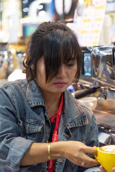 Bangkok, Thailand - June 3, 2017 : Unidentified woman barista pouring latte froth to make a coffee latte art into the white coffee cup for serve to customers in the coffee shop.