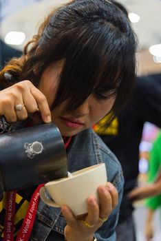 Bangkok, Thailand - June 3, 2017 : Unidentified woman barista pouring latte froth to make a coffee latte art into the white coffee cup for serve to customers in the coffee shop.