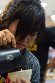 Bangkok, Thailand - June 3, 2017 : Unidentified woman barista pouring latte froth to make a coffee latte art into the white coffee cup for serve to customers in the coffee shop.