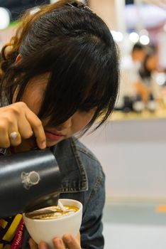 Bangkok, Thailand - June 3, 2017 : Unidentified woman barista pouring latte froth to make a coffee latte art into the white coffee cup for serve to customers in the coffee shop.