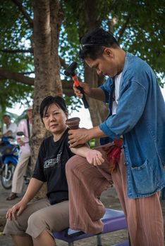 Bangkok, Thailand - July 28, 2017 : Unidentified Thai woman to take of service Thai massage by wooden hammer for treat aches and pains. The service comes in the outdoor garden.