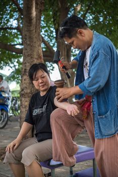 Bangkok, Thailand - July 28, 2017 : Unidentified Thai woman to take of service Thai massage by wooden hammer for treat aches and pains. The service comes in the outdoor garden.