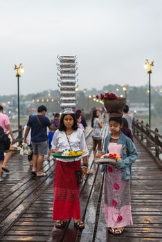 Kanchanaburi, Thailand - March 2, 2018 : Mon woman carry bowl on the head for transport walking on Mon Bridge, Wooden Bridge in Tambon Nong Lu, Amphoe Sangkhla Buri, Chang Wat Kanchanaburi