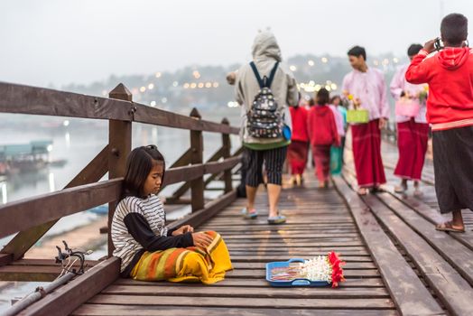 Kanchanaburi, Thailand - March 2, 2018 : Mon child woman sale flowers gatland in wood stick on Mon Bridge, Wooden Bridge in Tambon Nong Lu, Amphoe Sangkhla Buri, Chang Wat Kanchanaburi