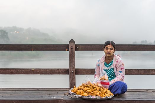 Kanchanaburi, Thailand - March 2, 2018 : Mon woman sale Samosa is snack fried filled puff with spicy sauce on Mon Bridge, Wooden Bridge in Tambon Nong Lu, Amphoe Sangkhla Buri, Chang Wat Kanchanaburi