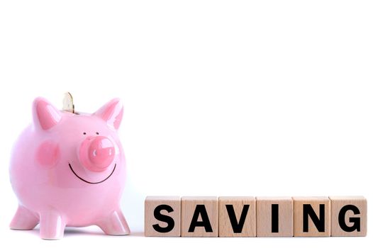 Pink piggy bank with falling gold coin with wooden block text. Isolated on white background. Saving concept.