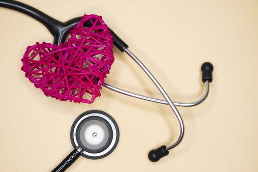 A black medical stethoscope and a red handmade rattan heart, isolated on light yellow background