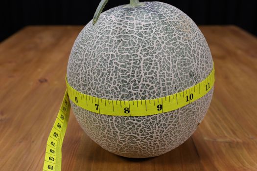 A cantaloupe melon and a yellow measuring tape on a brown wood table