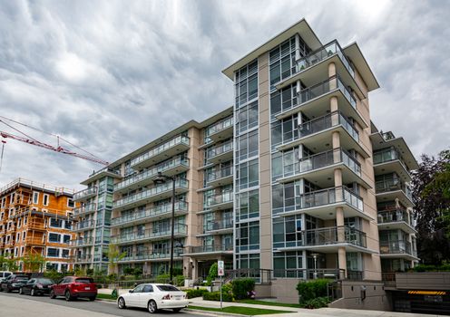 New residential low-rise building with cars parked on the street in front on cloudy sky background