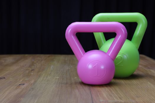 profile view of a green kettlebell for excerising and a large melon on a brown wooden floor