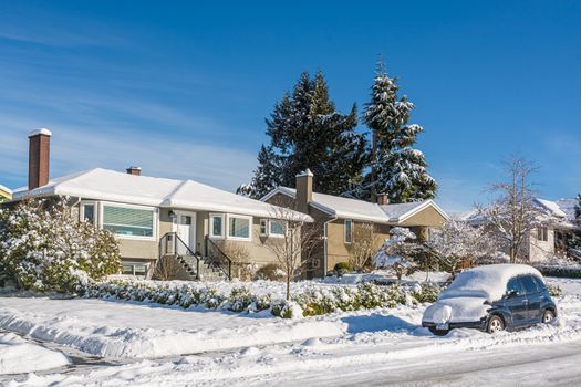 Snow covered residential house with car in snow on the road. Family house in snow on bright winter day