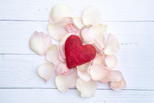 A red paper mache heart on a bed of pink rose petals