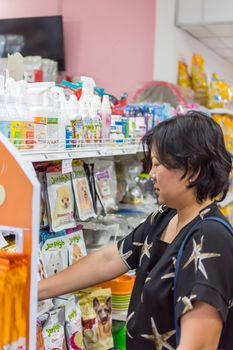 Bangkok, Thailand - June 28, 2016 : Customer woman shopping by selecting a variety accessories or pet food from pet goods shelf in petshop for her dog open daily for service everyday.