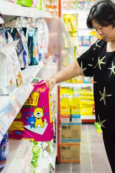 Bangkok, Thailand - June 28, 2016 : Customer woman shopping by selecting a variety accessories or pet food from pet goods shelf in petshop for her dog open daily for service everyday.