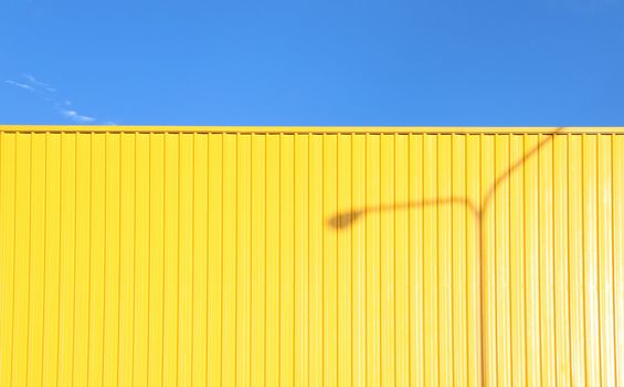a bright yellow metal wall reflexing the afternoon sun with a shadow of a light pole casting on it