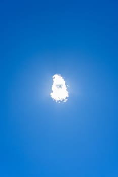 Cloud directly covering the sun and sunlight in a clean blue sky. Centered concept, solitude, unique, sunlight, blue color, tranquility, peace.