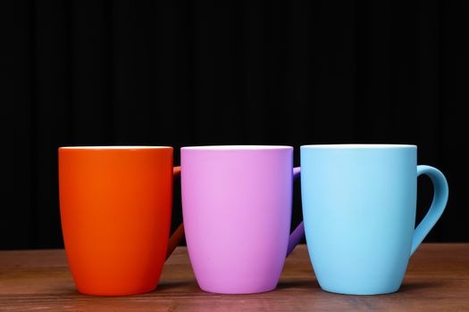 colorful coffee mugs on brown wood table top with black background