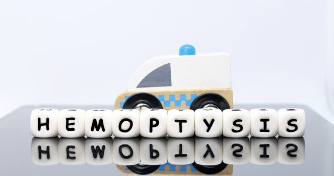 image of letters spelling a word hemoptysis and a model ambulance on a reflecting background