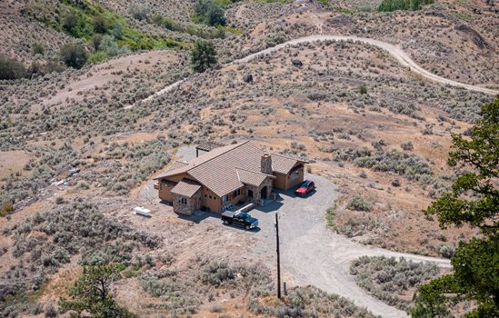 Residential house with cars parked beside in the middle of desert with gravel road near by