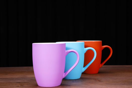 colorful coffee mugs on brown wood table top with black background