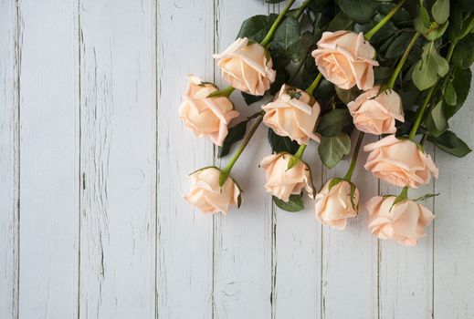Flat view image of a bouquet of peach color roses, on white wooden background