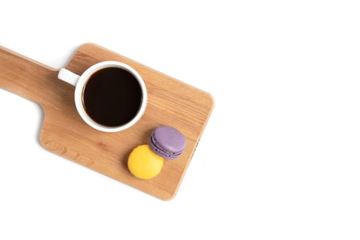 Colorful macaroons and a white ceramic cup of black coffee on a brown wooden cutting board. Isolated on whire background.