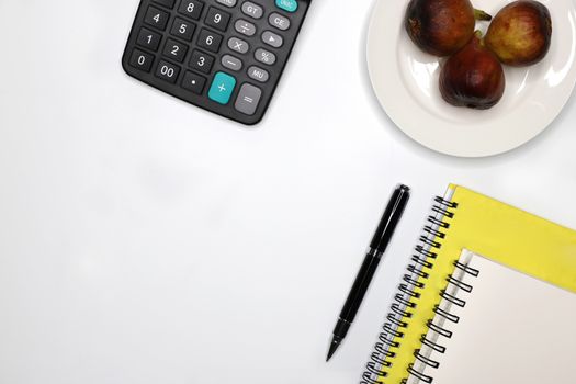 high angle view of a clean business desk top showing two notebooks, a calculator, a black pen, and a fruit plate