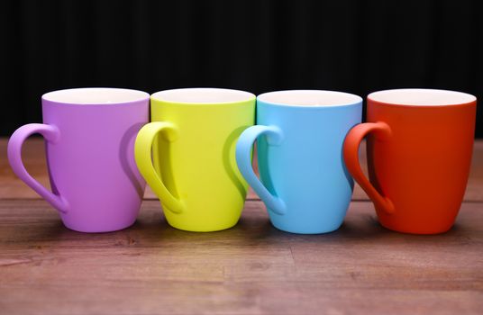 4 color full coffee mugs on a natural wood table top with black background