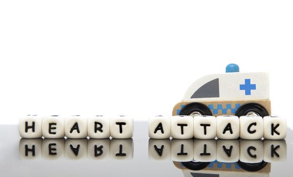 Alphabet letters spelling the word heart attack and a wooden toy ambulance. White background. Emergency medicine concept.