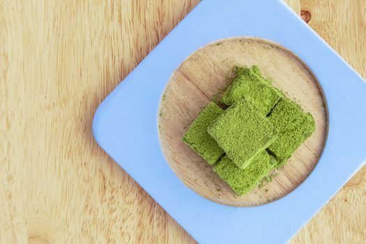White chocolate fudge heavily coated with fine green tea powder. Brown wooden background.