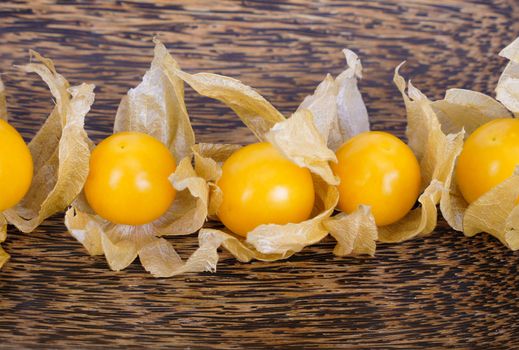 top view of ripe bright yellow cape gooseberries on brownish palmwood tray