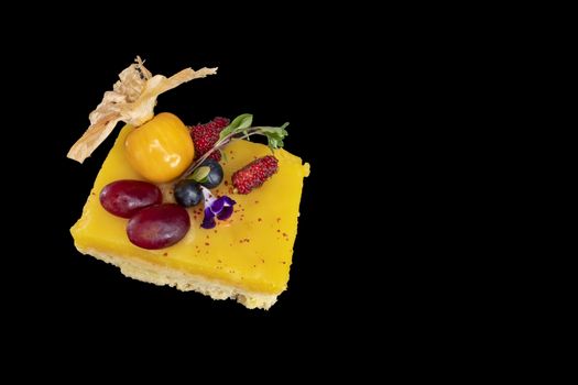A piece of colorful lemon custard shortbread with fresh mixed fruits isolated on dark black background. Closeup top view.