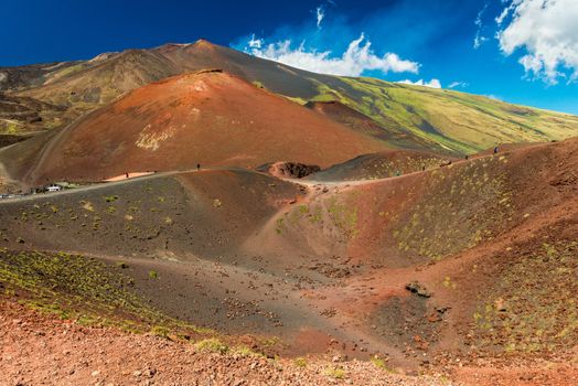 Beautiful landscape with lava hills covered with grass, a volcanic crater and people walking around it. Mount Etna, Sicily, Italy