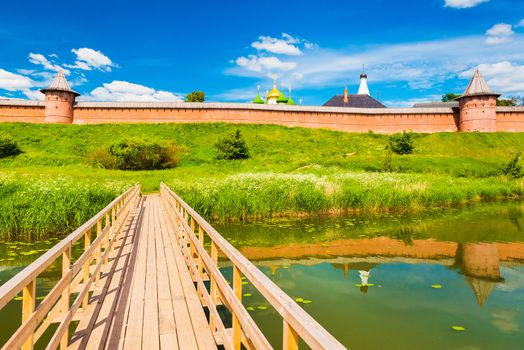 Suzdal cityscape with old Russian architecture. Wooden bridge across the river. The Golden Ring of Russia. Old town reflected in water of the Kamenka River.