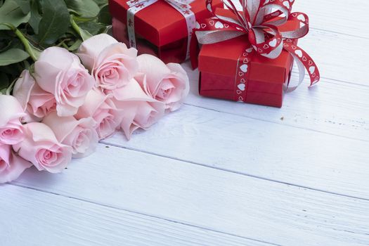 Beautiful bouquet of pink roses and red present boxes on pale blue-colored wood background. Selective focusing. Love, Romance, Valentine's Day, Anniversary.