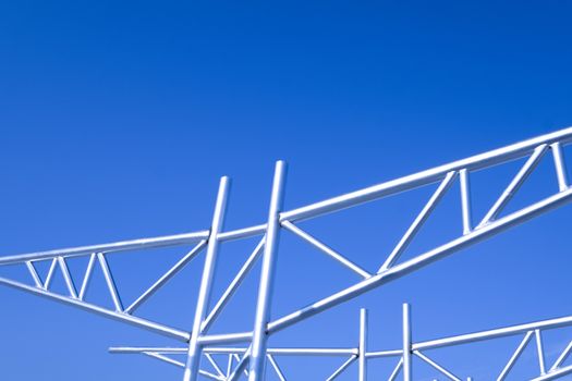 Strong shiny metal truss frames with joists, bridges, struts, joints, and poles for garage roof supports. Perspective view against bright blue sky