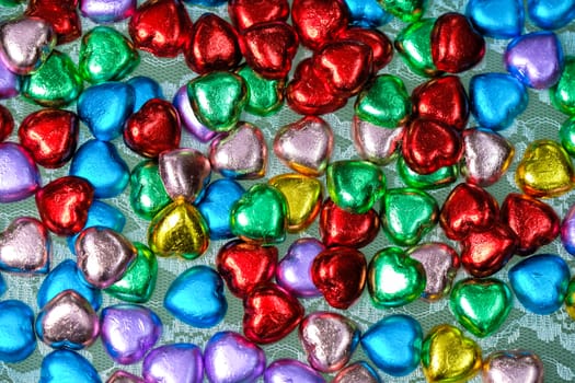 heart-shaped chocolate candies in various colors on white lace background, Valentines' Day, romantic concept, top view