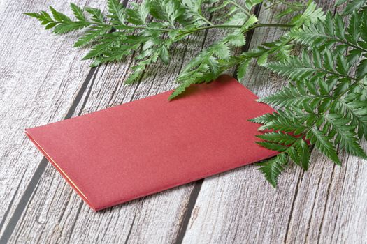 Fresh rainforest ferns and a red invitation card on brown wood background. Mock up template design. Copy space