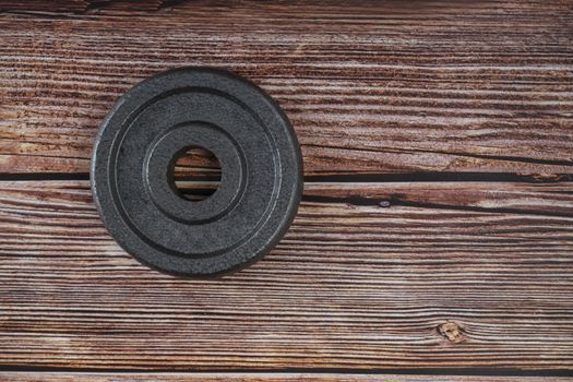 A metal weight plate on brown wooden background.